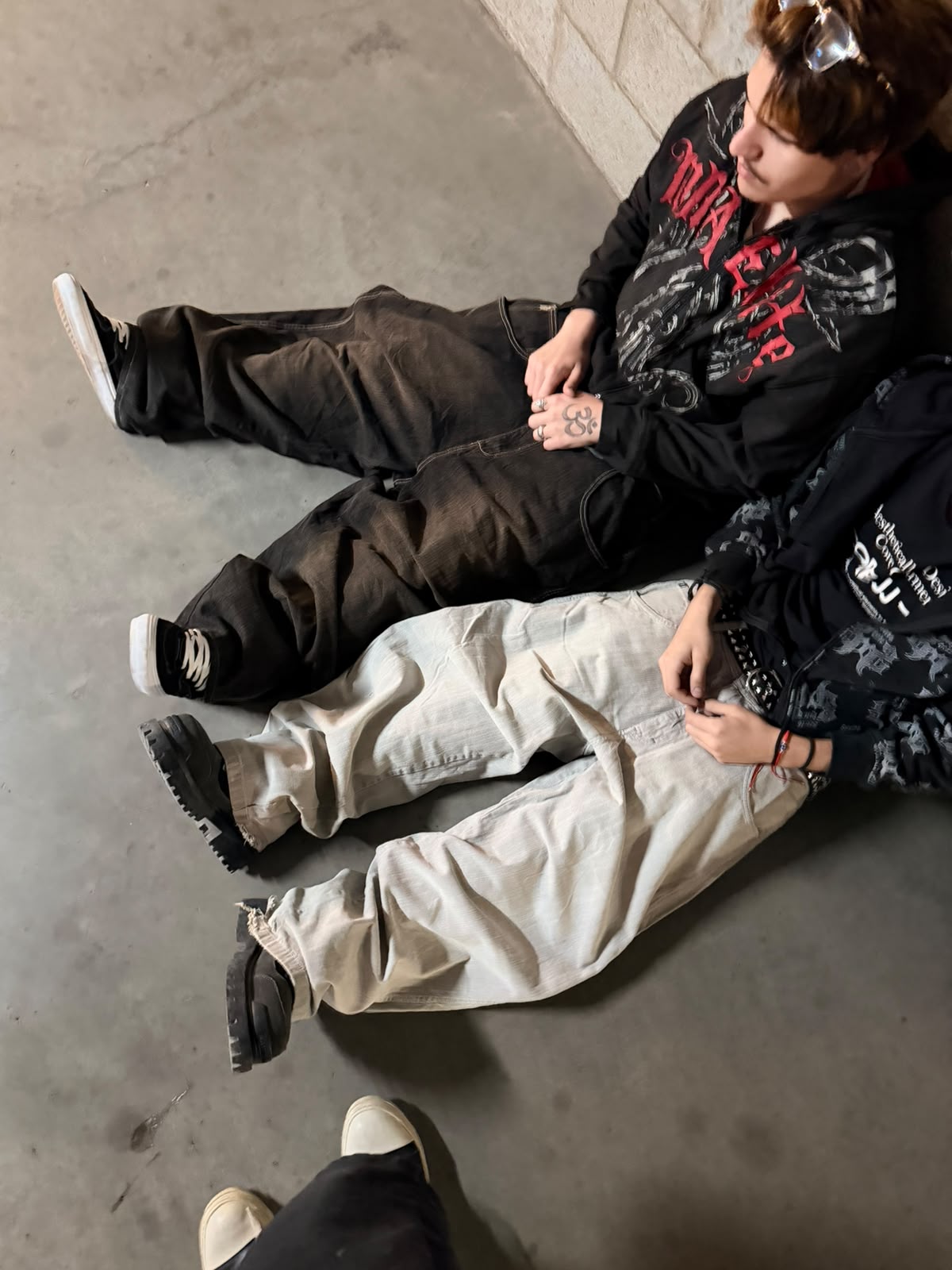 Dos personas sentadas con jeans baggy y hoodies