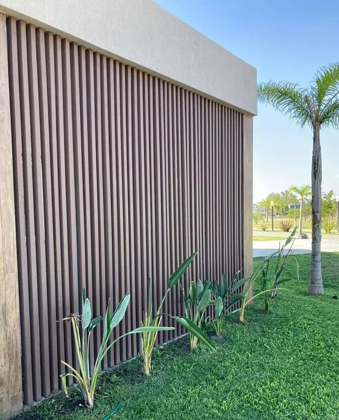 Muro exterior revestido en columnas WPC Vankka color Cedro colocadas en vertical junto a un jardín