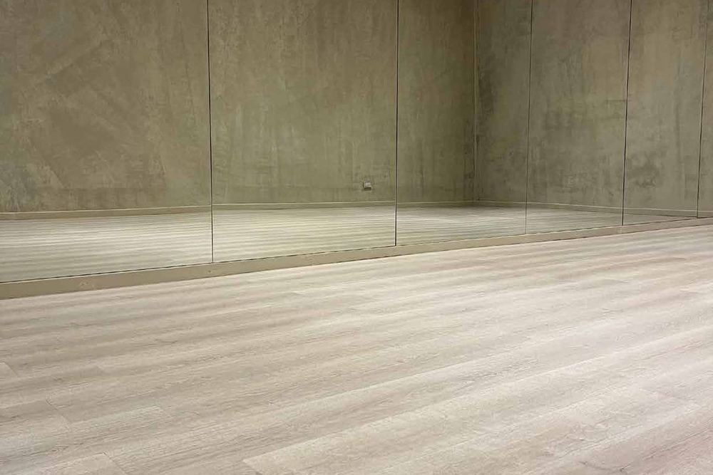Piso flotante HDF símil madera en tono claro ya instalado en un salón amplio con espejos