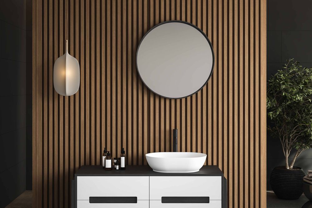 Baño con la pared revestida en wall panel WPC símil madera detrás de un espejo redondo y la bacha