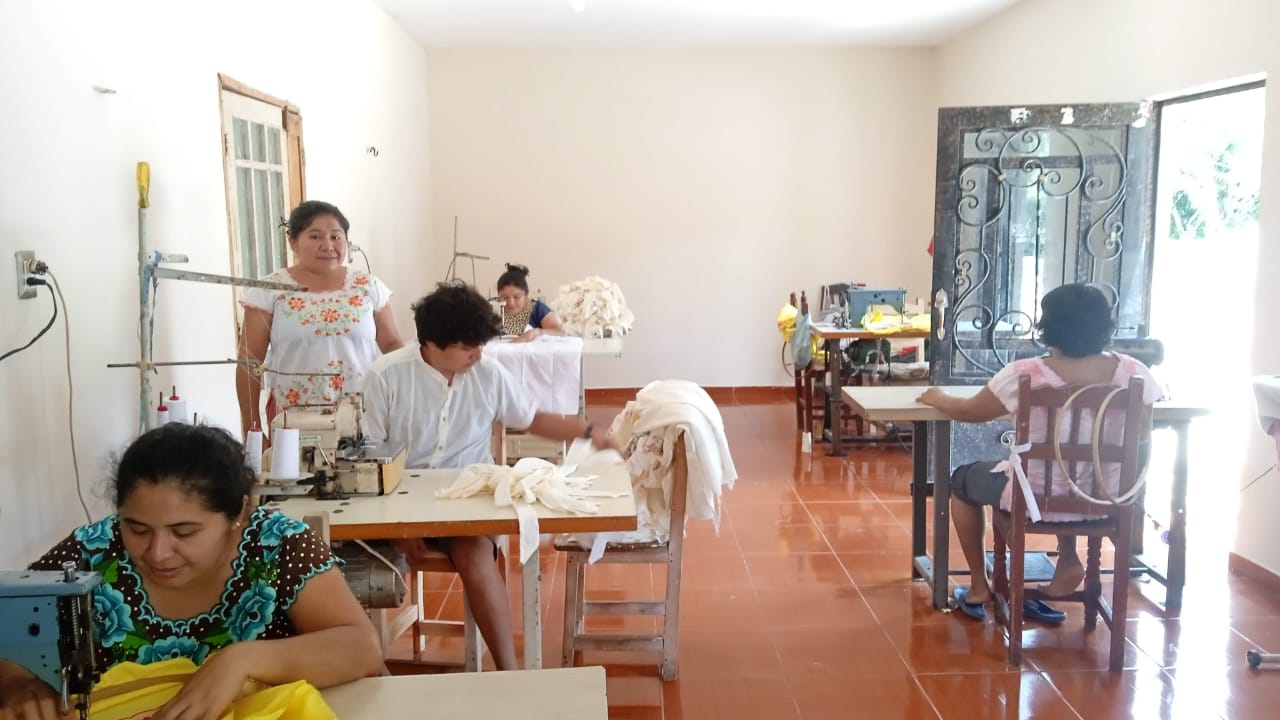 Taller Típicas Pat Carrillo en Kimbilá: artesanos y familia trabajando bordado en máquina 20U, corte y confección de hipiles.