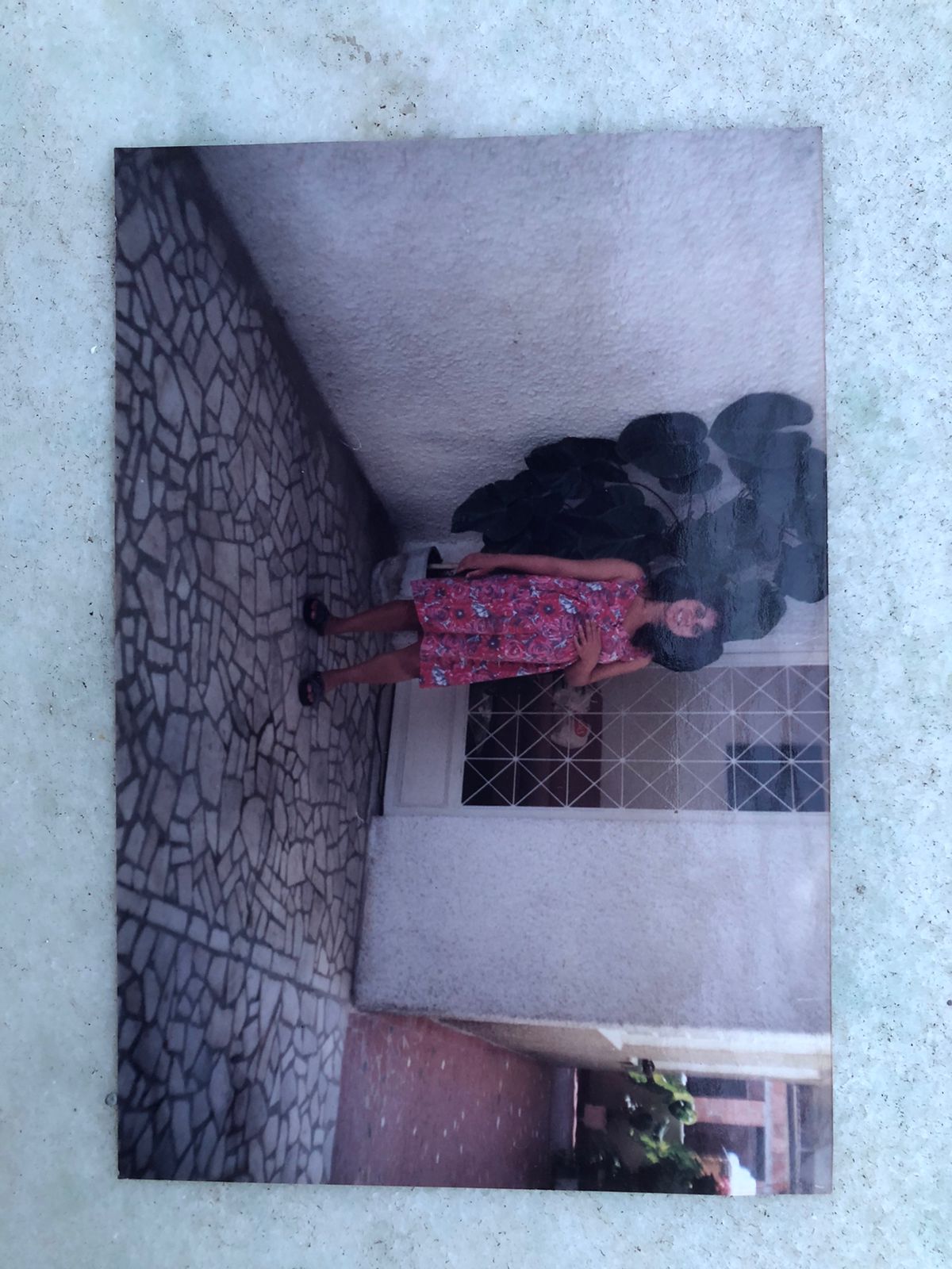 Mulher de vestido estampado diante de uma casa.