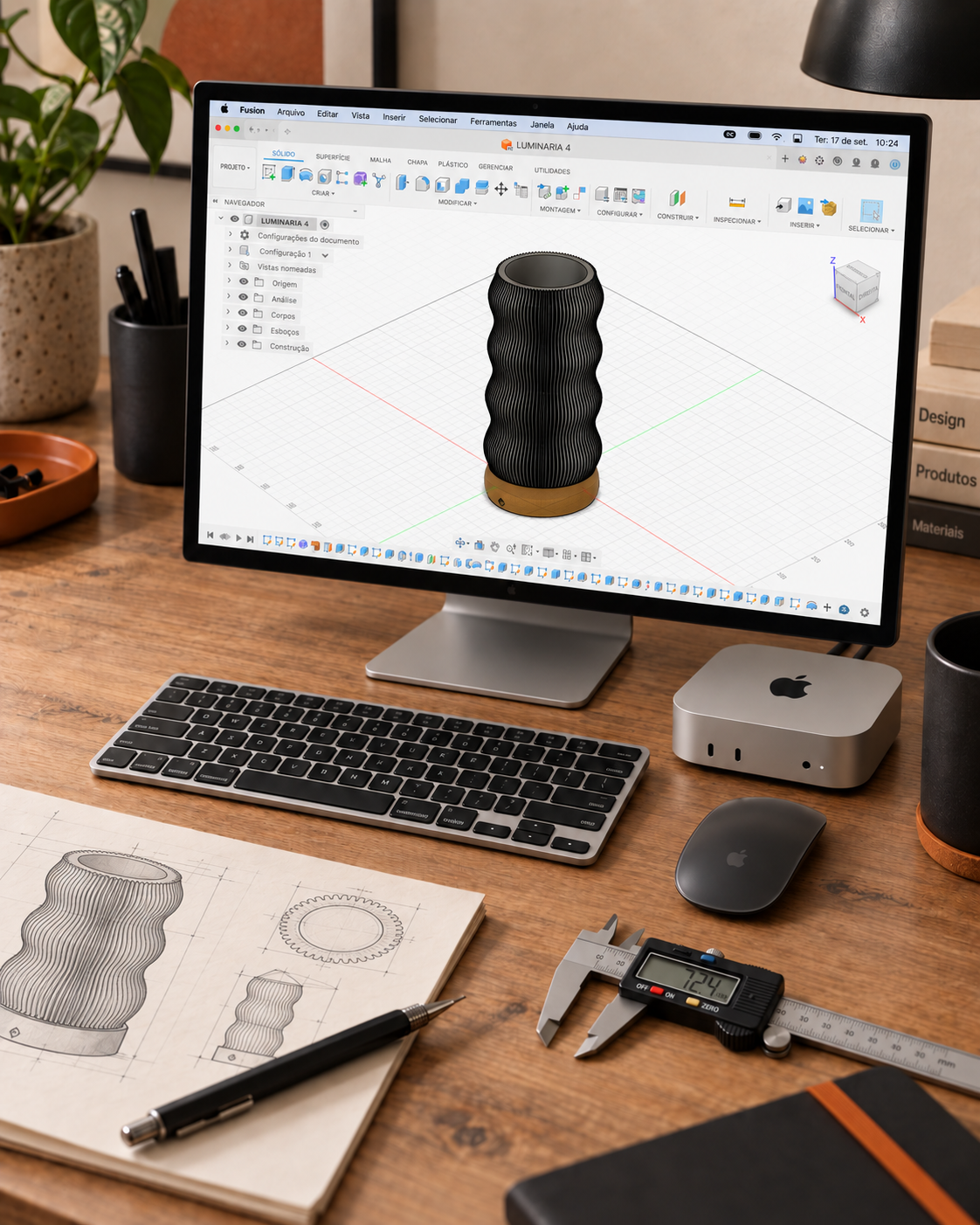 Representação de um projeto de luminária em um programa de modelagem 3D, com Mac mini, desenhos e paquímetro digital sobre a bancada.