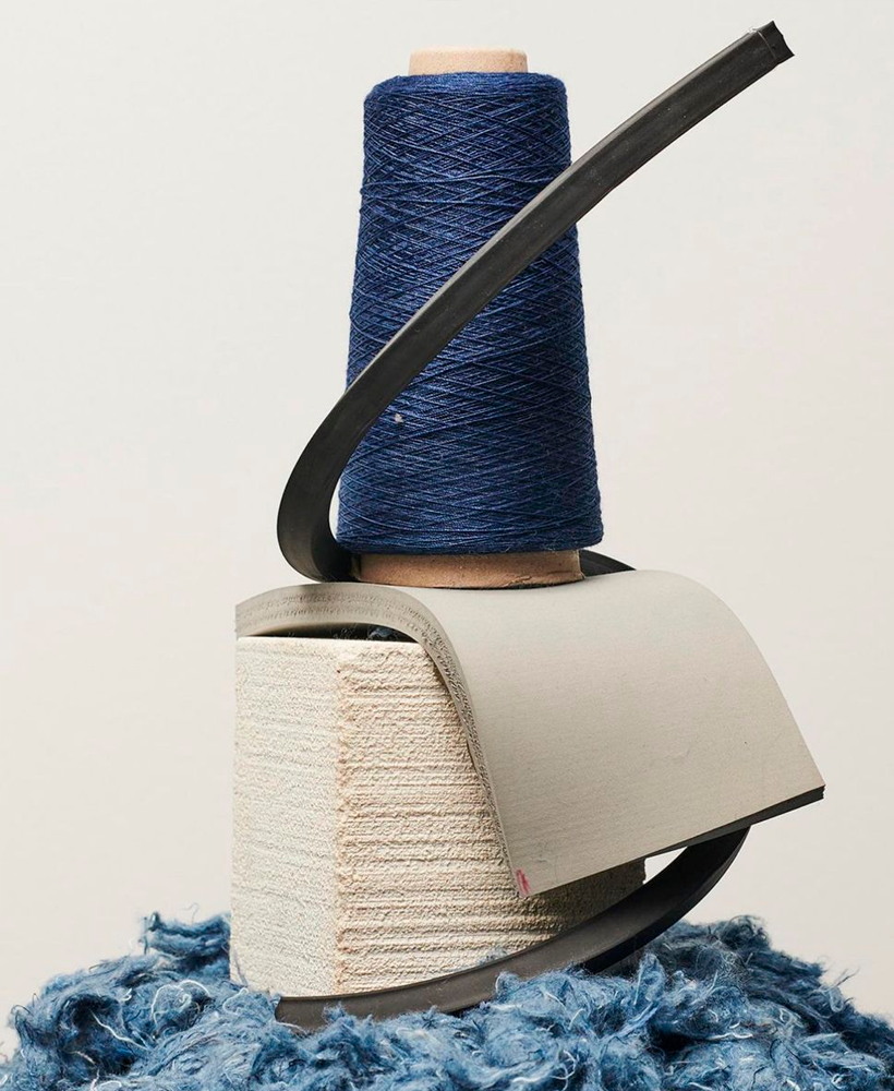 Indigo yarn cone resting on raw cotton and denim waste