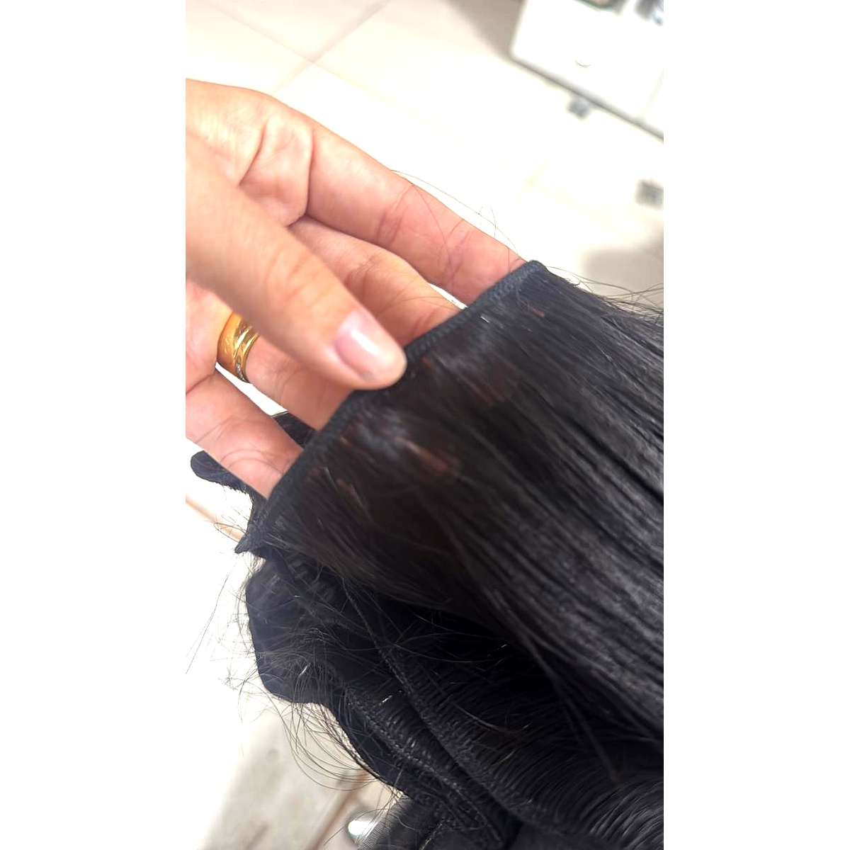 Mão segurando uma tela invisível de cabelo peruano andino castanho escuro já costurada, mostrando a faixa de costura.