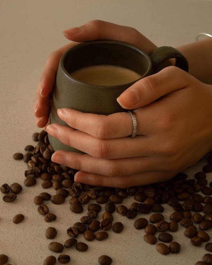 Manos sosteniendo una taza de café rodeada de granos de café