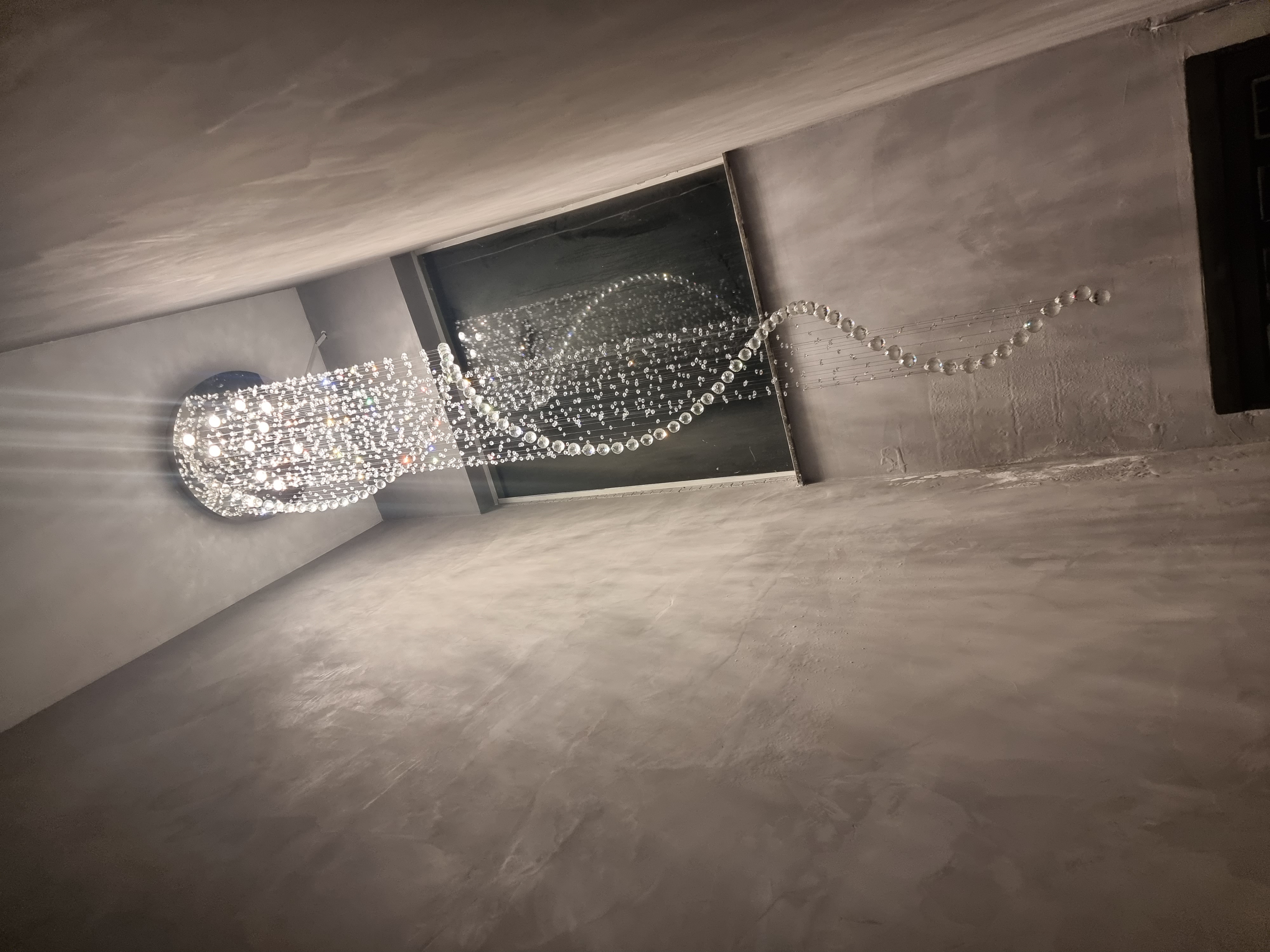 Lustre de cristal modelo "Caracol" da Linha Kria instalado em ambiente com pé direito duplo, com cristais K9 legítimos em espiral decorando sala de estar moderna.