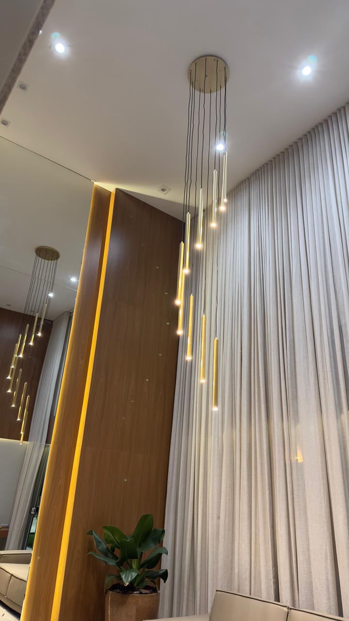 Imagem de um lustre da Linha Ming Dourado, com hastes longas e douradas penduradas em um suporte preto.