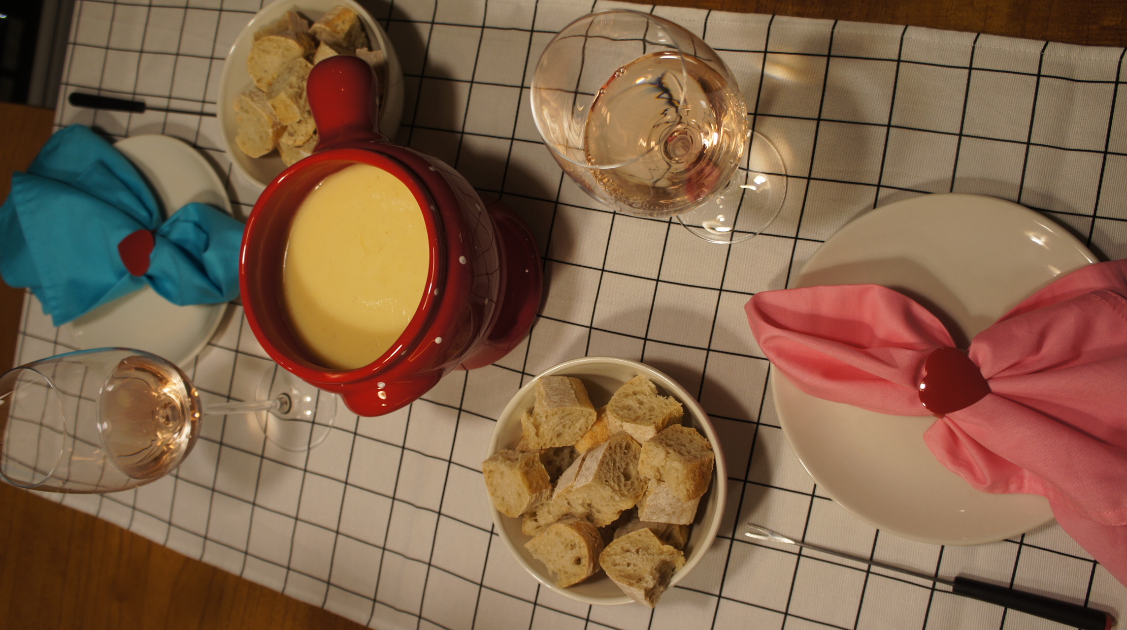 Mesa posta com fondue, vinho e guardanapo rosa